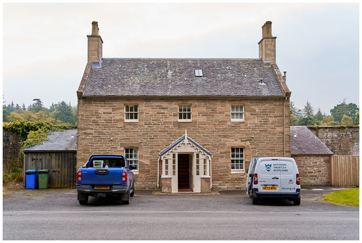 Stone cottage with two vehicles parked in front and chimneys on the roof.