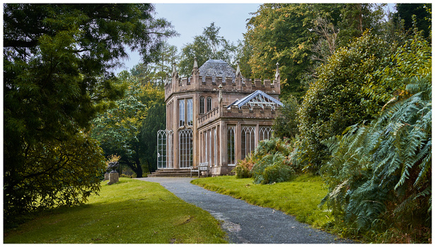 Gothic Revival stone building with turrets nestled among mature trees along a curved pathway.