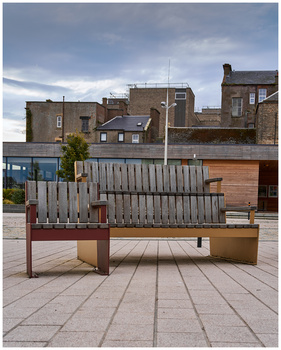 Modern wooden bench with geometric lattice backrest in urban plaza with period architecture.