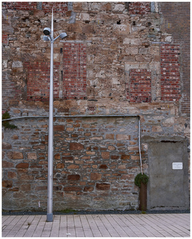 Weathered red brick wall with white pipe and metal fixtures in urban setting.