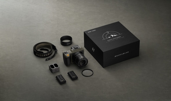 Hasselblad camera system with interchangeable lenses, accessories, and black branded box displayed on gray surface.