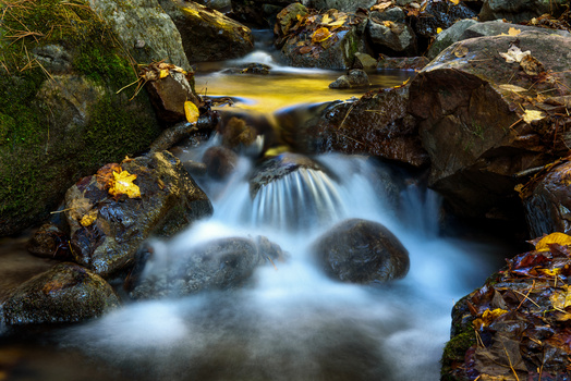 Mountain stream with silky flowing water cascading over moss-covered rocks and boulders.