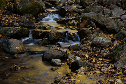 Long exposure photograph of a rocky mountain stream with silky flowing water and moss-covered boulders.