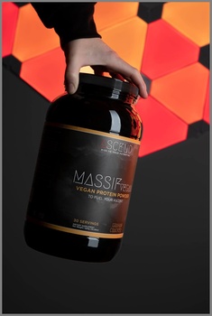 Hand holding a dark amber glass bottle with gold accents against a geometric hexagonal background in warm tones.