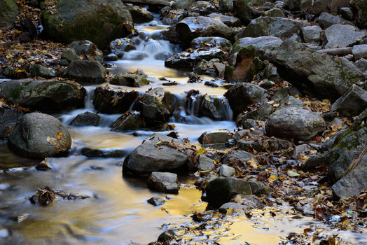 Mountain stream flowing over moss-covered rocks with long exposure blur effect.