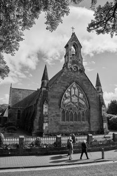 Gothic Revival chapel with ornate stonework and rose window, framed by tree branches in black and white.