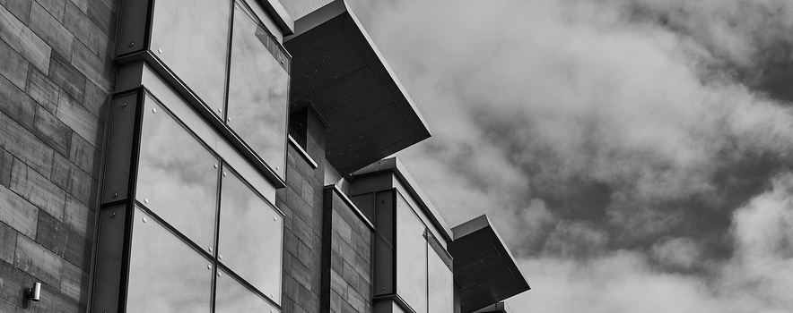 Modern building facade with rectangular windows and dark sunshades against a dramatic cloudy sky.