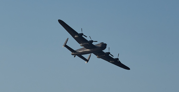 Avro Lancaster heavy bomber aircraft in flight against clear blue sky.
