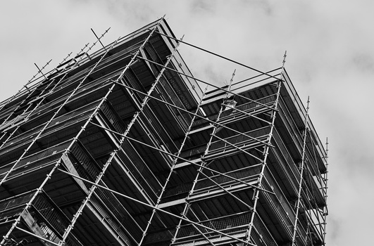 Tall building under construction with metal scaffolding covering its facade against an overcast sky.