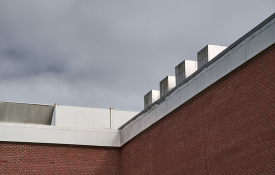 Brick building roofline with white parapet and rectangular ventilation vents against overcast sky.
