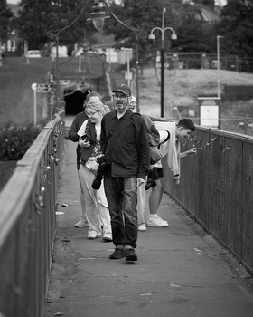 Three people walking on a narrow pedestrian footbridge in black and white.