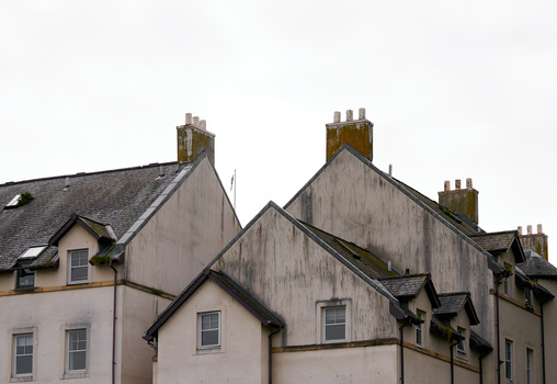 Row of traditional stone cottages with distinctive pitched rooflines and multiple chimneys against an overcast sky.