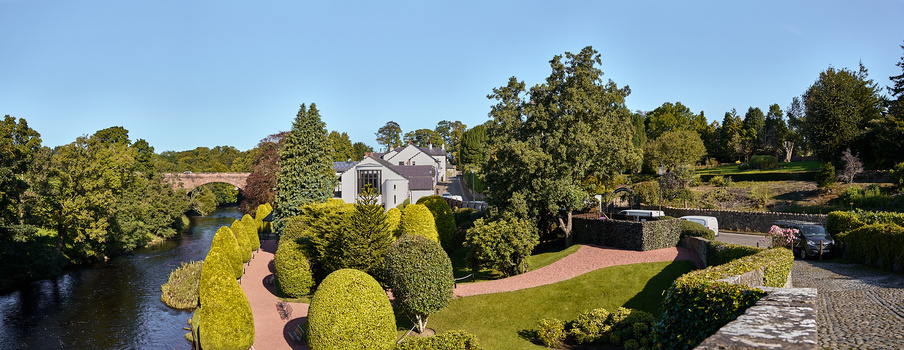Aerial view of a white house surrounded by manicured topiary and gardens beside a river.