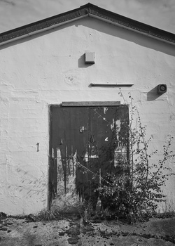 Weathered white-walled building facade with dark wooden door and mounted fixtures in black and white.
