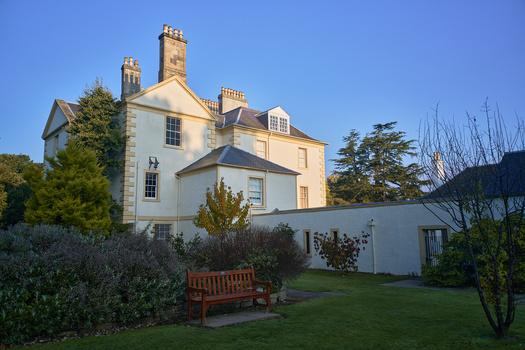 Two-story cream and white country house with multiple chimneys and dormer windows, illuminated by golden hour sunlight.