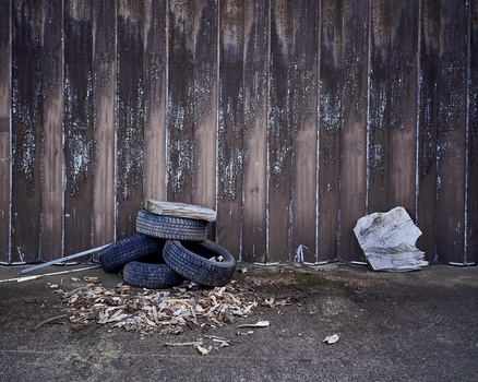 Discarded rubber tires and white plastic waste stacked against a weathered wooden wall.