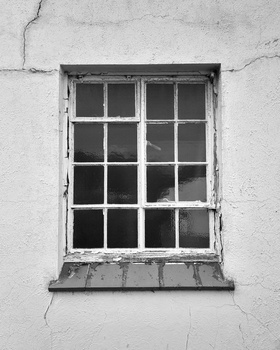 Weathered white wall with a 16-pane window featuring dark glass and peeling paint around the frame.