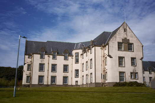 Large cream-colored Scottish castle with dark slate roof and multiple chimneys, set on manicured lawn.