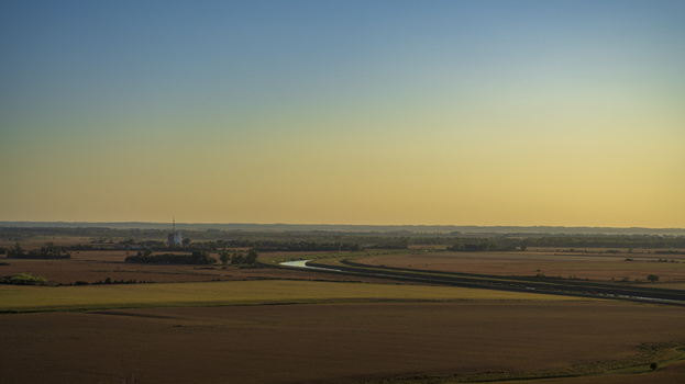Aerial view of expansive agricultural fields with a winding river under golden hour light.
