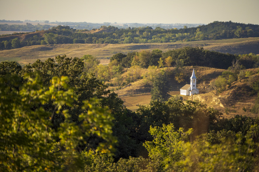White church with steeple nestled in rolling forested landscape under golden afternoon light.