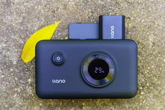 Liano instant camera in dark blue with yellow flash diffuser and two film cartridges displayed on sandy surface.
