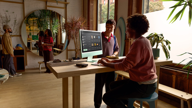 Creative professional working at standing desk with dual monitors in bright, plant-filled studio space.