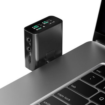 Compact black power bank with LED display mounted next to laptop keyboard.