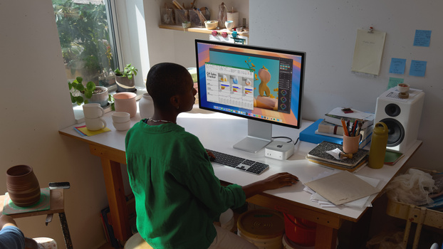 Person in green shirt seated at desk working on design project displayed on monitor.