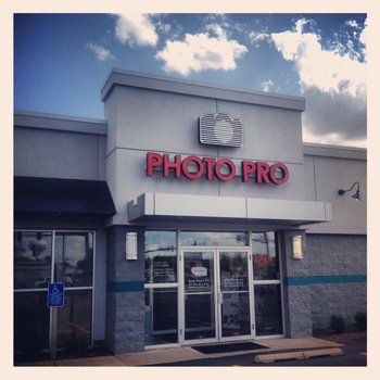 Storefront of Photo Pro retail location with red neon signage and glass entrance doors.