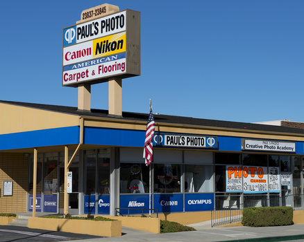 Storefront of Paul's Photo shop with large signage advertising Canon, Nikon, and carpet and flooring services.