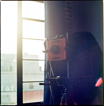 Large format camera silhouetted against bright window light in a studio setting.