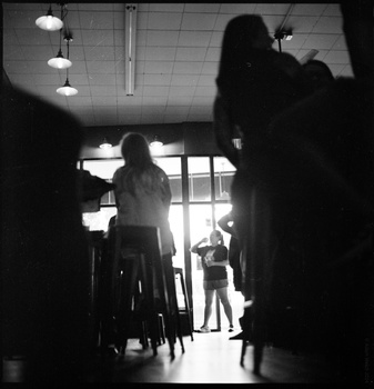 Silhouetted figures in a bright interior hallway with overhead lighting and large windows.