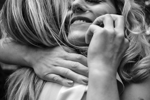 Black and white portrait of a smiling woman with long wavy hair, her hand touching her face and neck.
