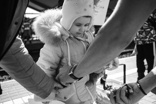 Small child in winter clothing held up by adults in black and white.