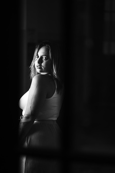 Woman in sleeveless top looking over shoulder against dark background with dramatic side lighting.