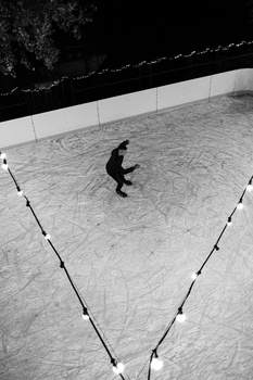 Overhead view of a figure in black clothing standing in the center of a geometric triangle marked by white boundary lines on pavement.