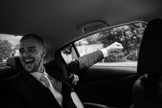 Man laughing in convertible car with arm extended, captured in black and white.