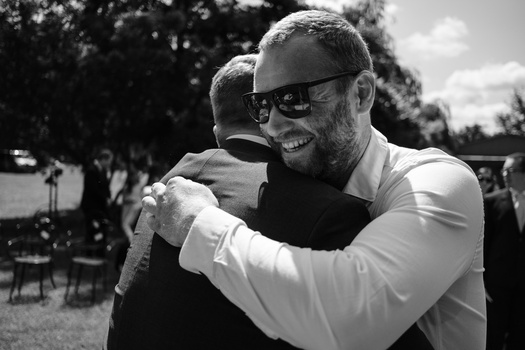 Man in sunglasses embracing another person outdoors in black and white.