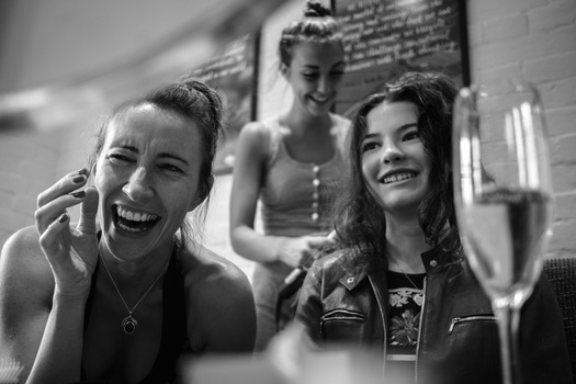Three women laughing together at what appears to be a celebration, shot in black and white.