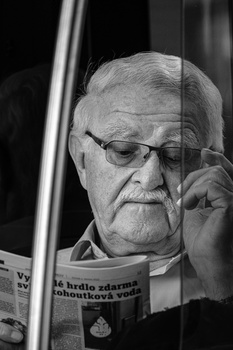 Elderly man wearing glasses reads a newspaper in profile, shot in black and white.