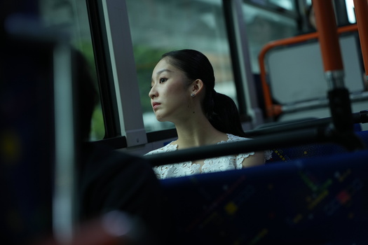 Woman gazing out a bus window, lit by natural light filtering through glass.