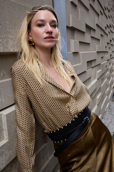 Woman in knit sweater and leather skirt posed against textured concrete wall.