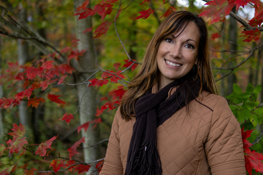 Woman smiling at camera surrounded by red autumn foliage in a forest setting.