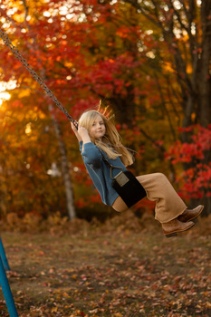 Young child on a swing with vibrant autumn foliage in soft, golden backlit lighting.