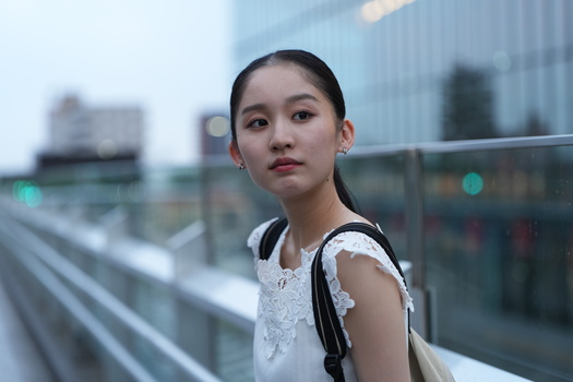 Young woman in white lace top looking over shoulder against urban glass building backdrop.