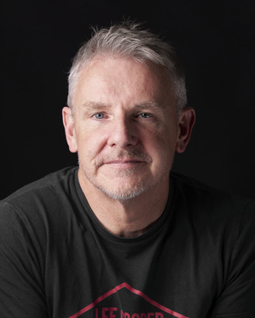 Headshot of a middle-aged man with gray hair against a black background.