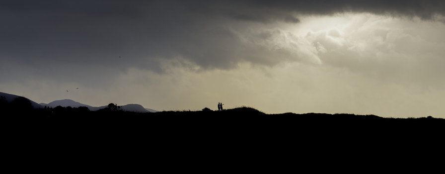 Silhouetted landscape with dark hillsides beneath dramatic storm clouds and crepuscular rays.
