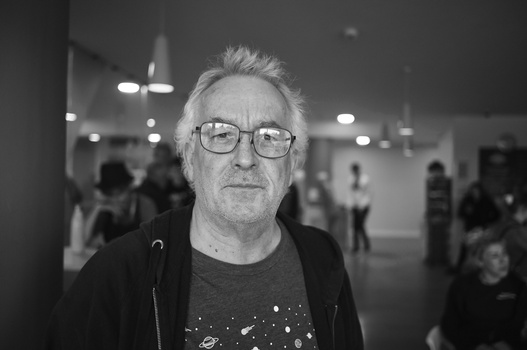 Man wearing glasses and dark jacket in indoor venue with bokeh lighting in background.