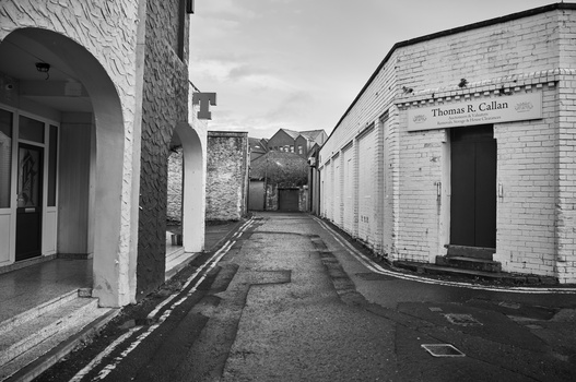 Narrow wet alleyway between white brick buildings under overcast sky.