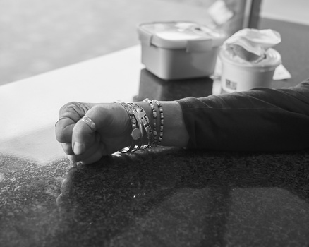 Hand resting on dark surface wearing multiple beaded bracelets, black and white photograph.